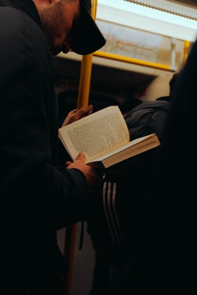 Homme lisant un livre dans un train, entouré de personnes.