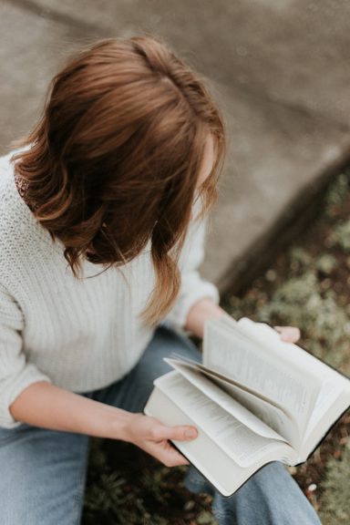 Une personne lit un livre assise sur le sol, vêtue d'un pull blanc.